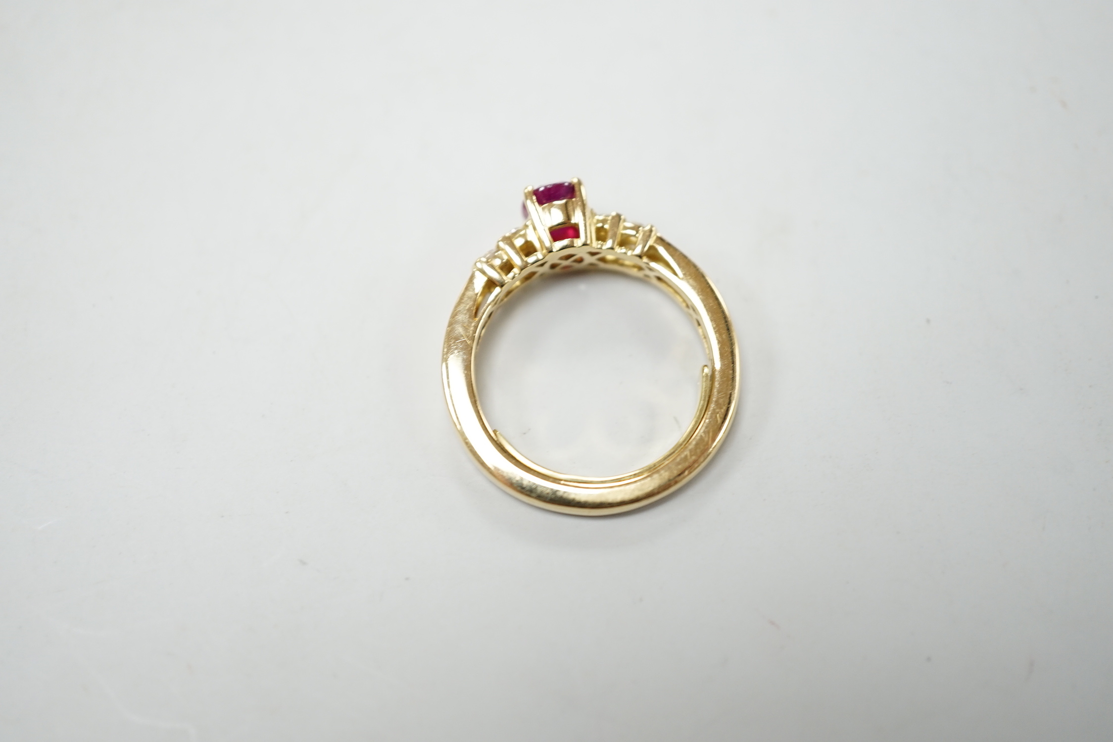 A modern yellow metal and single stone oval cut ruby set dress ring, with ten stone diamond chip set shoulders, size M, gross weight 5.7 grams.